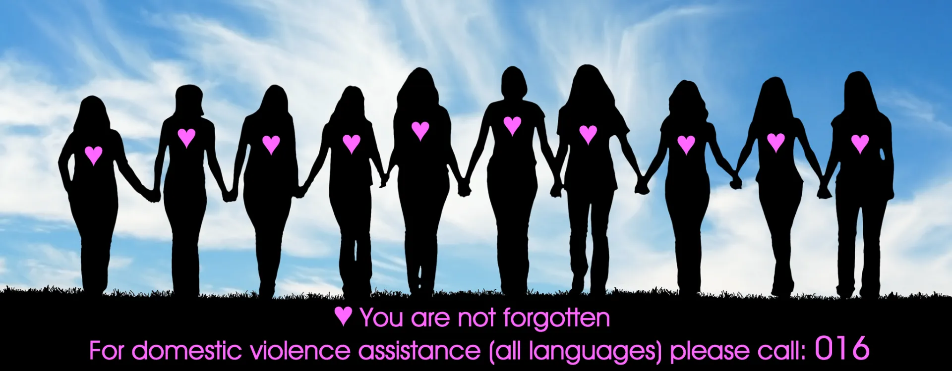 Siluetas de mujeres cogidas de la mano bajo un cielo azul, con un texto en inglés: «You are not forgotten. For domestic violence assistance (all languages) please call: 016». Quiere decir: nadie te olvida; si sufres violencia doméstica, llama al 016, en cualquier idioma.