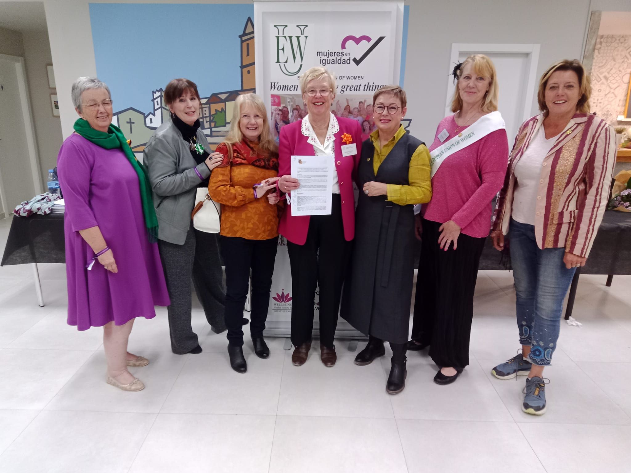 Siete mujeres de la asociación ante la pancarta de la EUW y Mujeres en Igualdad, una de ellas con un documento firmado